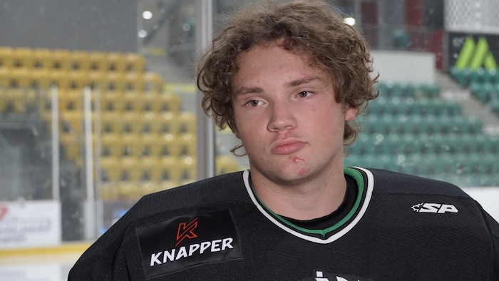 Un jeune joueur de hockey répond aux questions d'un journaliste pendant une entrevue devant des gradins vides.