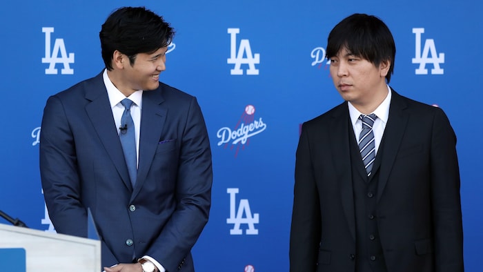 Deux hommes en veston se tiennent debout devant le logo des Dodgers.