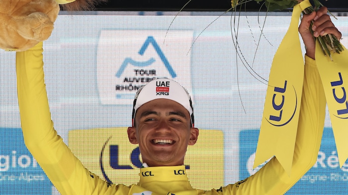 Vêtu d'un maillot jaune, il lève les bras au ciel pour célébrer sa victoire, tout sourire.