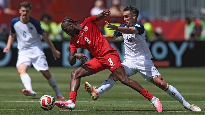 Un joueur de soccer en rouge se défait d'un adversaire en blanc.