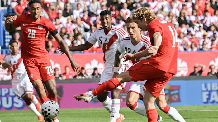 Un joueur de soccer botte le ballon devant deux adversaires et un coéquipier.