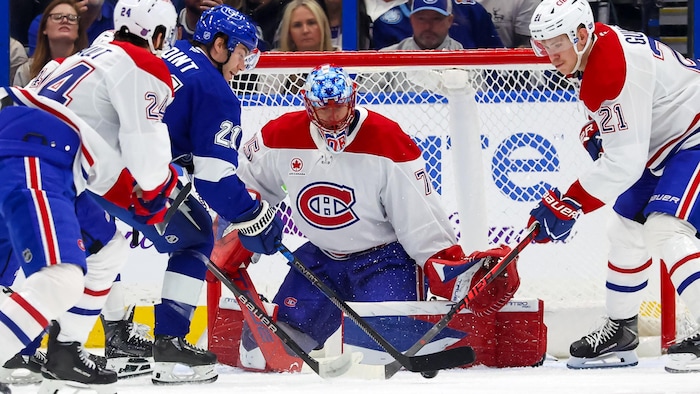 Des joueurs de deux équipes de hockey se disputent la rondelle devant un gardien.