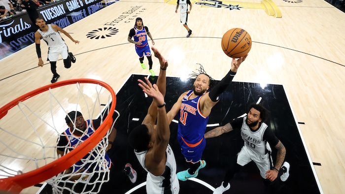 Un basketteur tente un tir, entre deux adversaires, près du panier.
