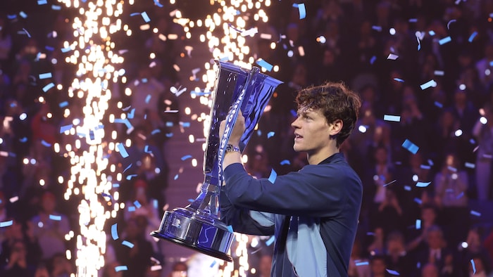 Un joueur de tennis lève un gros trophée alors que des confettis tombent et que des étincelles jaillissent.