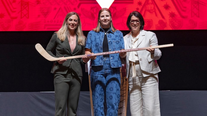Trois femmes posent devant l'appareil photo avec un bâton de hockey dans les mains.