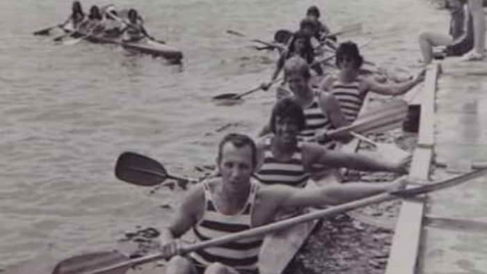 Photo en noir et blanc de quatre kayakistes qui s'approchent d'un quai à la fin d'une course. 