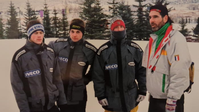 Quatre hommes posent pour la caméra, l'hiver, à l'extérieur.