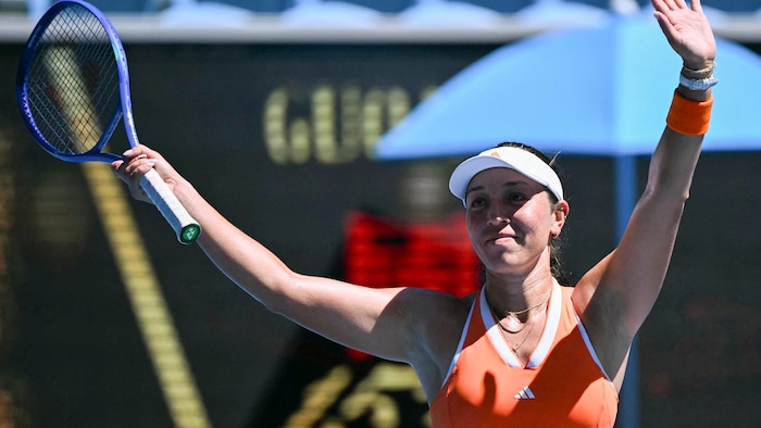 Une joueuse de tennis lève les bras et sourit.