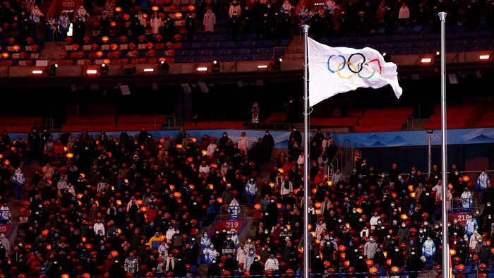 Un drapeau affichant les cinq anneaux olympiques flotte au vent.