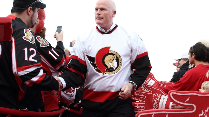 Un homme avec un chandail de hockey blanc marche dans une foule.