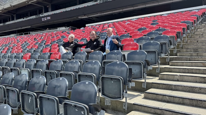 Trois dirigeants de football discutent dans les gradins.