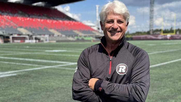 Un dirigeant d'équipe de football est tout sourire devant un terrain.