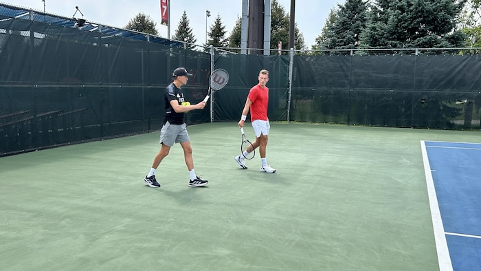 Les deux hommes discutent et marchent sur un terrain d'entraînement.
