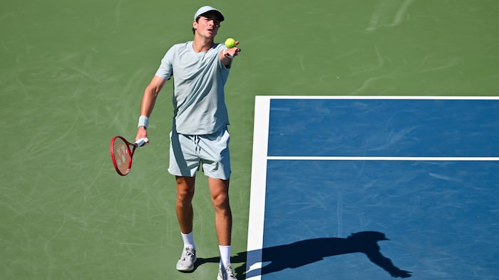 Un joueur de tennis en vert s'apprête à lancer sa balle avant un service. 