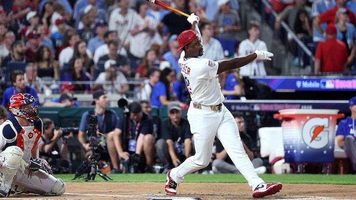 Un baseballeur termine son élan au bâton et regarde au loin.