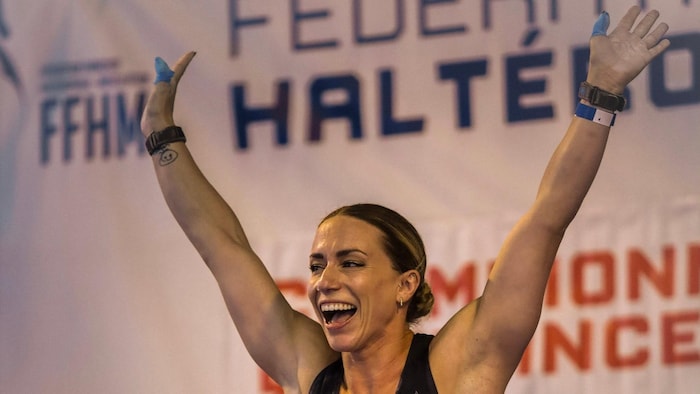 Femme en maillot d'haltérophile lève les bras en l'air.