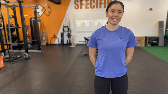 Une jeune athlète prend la airs dans un gymnase vêtue d'un chandail bleu.