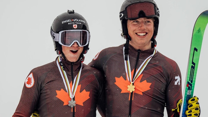 Deux skieurs casqués sourient avec leurs médailles autour du cou. 