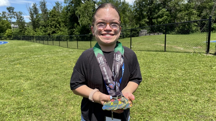 Une adolescente souriante tenant ses médailles.