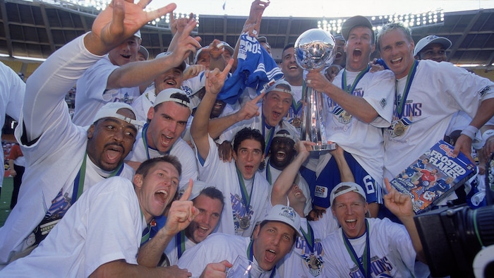 Des joueurs de soccer vêtus de blanc célèbrent la conquête d'un championnat avec le trophée et une médaille au cou.