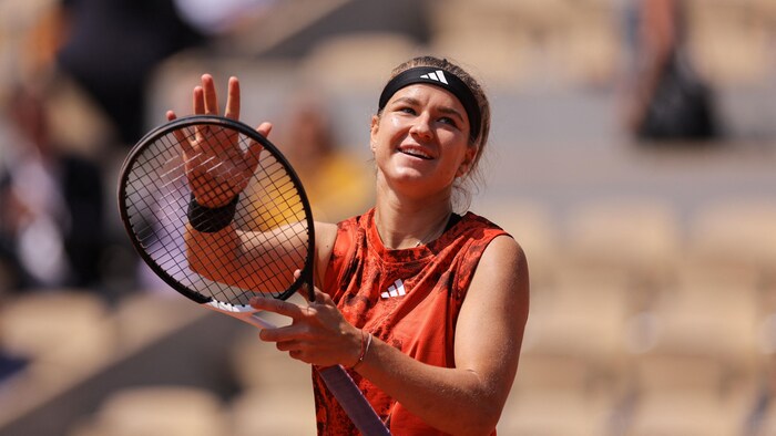 Une joueuse de tennis sourit et applaudit avec sa raquette en regardant la foule.
