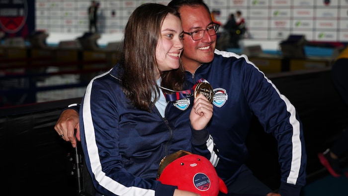 Une femme, accompagnée de son entraîneur, présente fièrement sa médaille.
