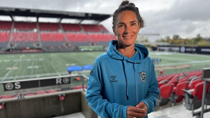 Une entraîneuse de shot    vêtue de bleu rend la airs  determination    la caméra dans les gradins d'un stade. 