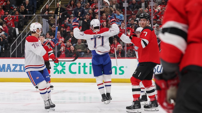 Un joueur de hockey célèbre son but devant des adversaires.