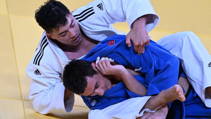 Deux judokas, par terre, se battent sur un tatami.