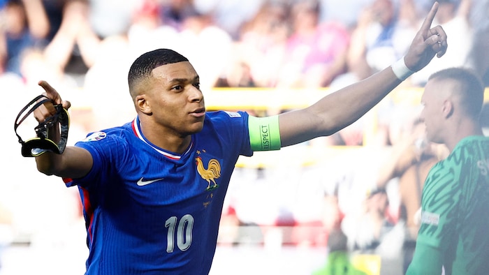Un joueur de soccer en bleu lève les bras pour célébrer un but.
