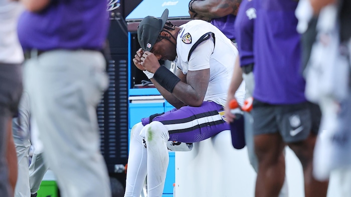 Un footballeur est assis sur le banc et tient sa casquette.