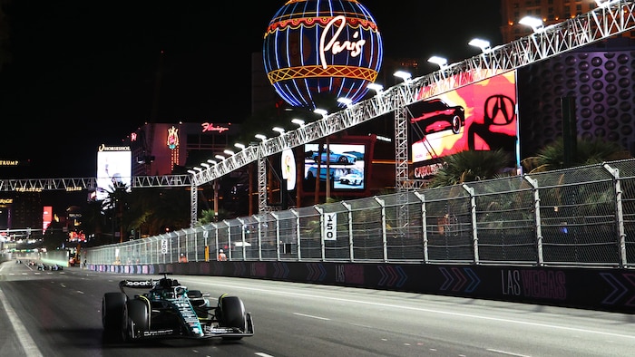 Une monoplace roule de nuit sur un circuit illuminé par des affiches publicitaires, entre des grillages de sécurité.