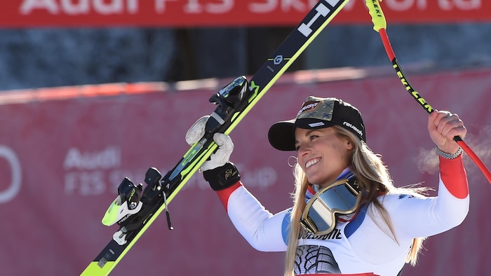Elle sourit en soulevant ses skis. 