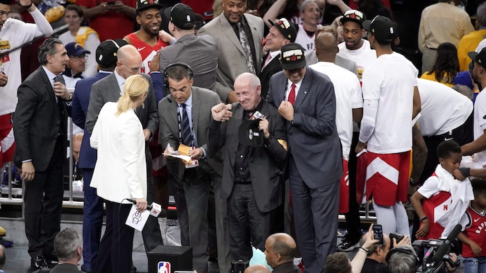 Un homme serre les poings et lève les bras dans les airs en signe de célébration. Il est entouré de joueurs de basketball.