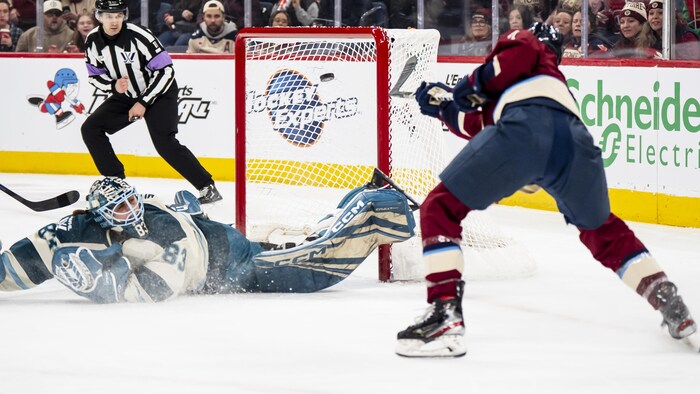 Une joueuse de hockey marque un but alors que la gardienne est allongé sur la patinoire. 