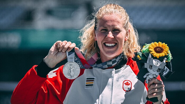 Une femme sourit en brandissant une médaille d'argent.