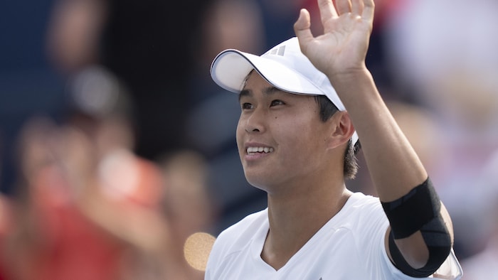 Un jeune joueur de tennis salue la foule, tout en souriant.