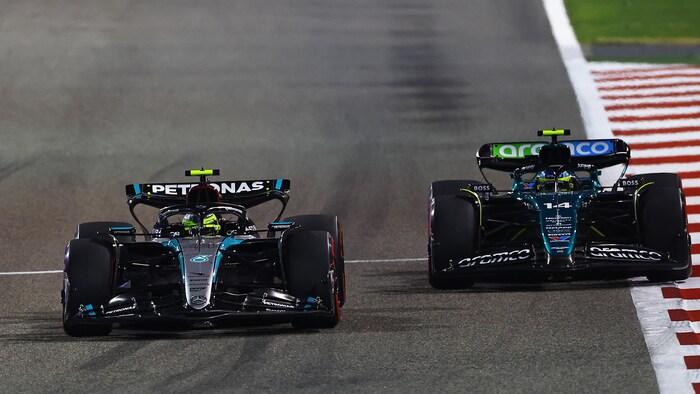 Deux monoplaces F1, de face, se font la lutte sur un circuit éclairé.