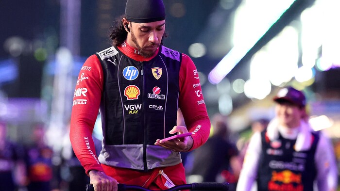 Une main sur le guidon de sa trottinette, un homme regarde son téléphone cellulaire.