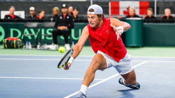 Un joueur de tennis frappe une balle du revers de sa raquette.