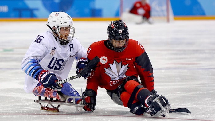 Le Canadien, pourchassé par le joueur des États-Unis, protège la rondelle.