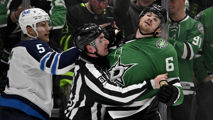 Un arbitre sépare deux hockeyeurs lors d'un match.