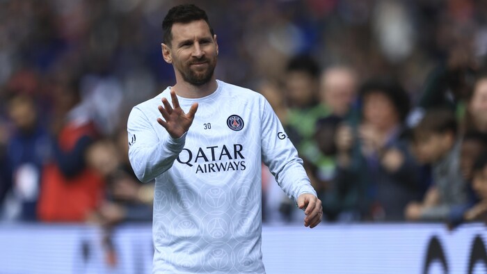 Un joueur de soccer fait un geste de la main en souriant pendant un match.