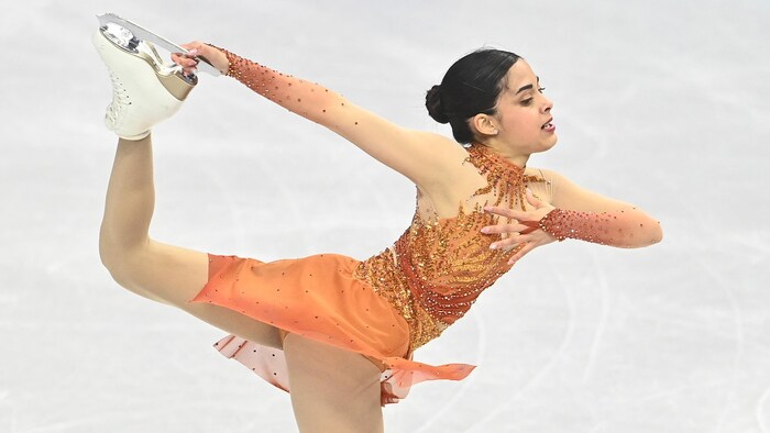 Une patineuse artistique effectue une pirouette avec le pied dans la main.