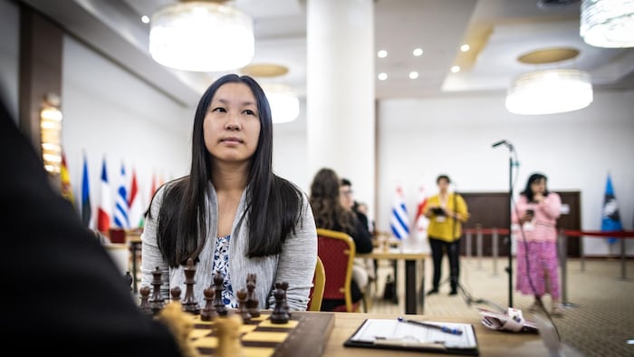 Elle est assise devant un jeu d'échecs.
