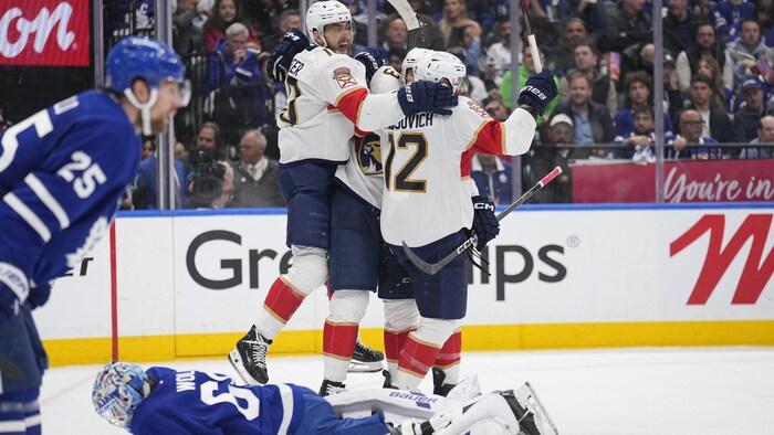 Des joueurs de hockey célèbrent un but devant deux adversaires, dont le gardien qui est étendu sur la glace.