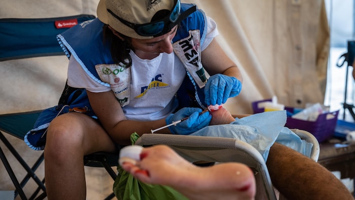 Une personne tient une seringue et un bandage au-dessus du pied ensanglanté d'un coureur.
