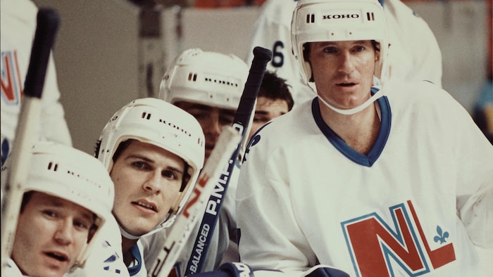 Marc Messier está apoyado contra las tablas frente al banquillo de jugadores de la selección de Quebec.