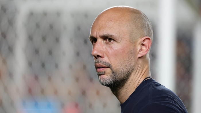 Gros plan sur le visage de l'entraineur-chef, qui regarde au loin.