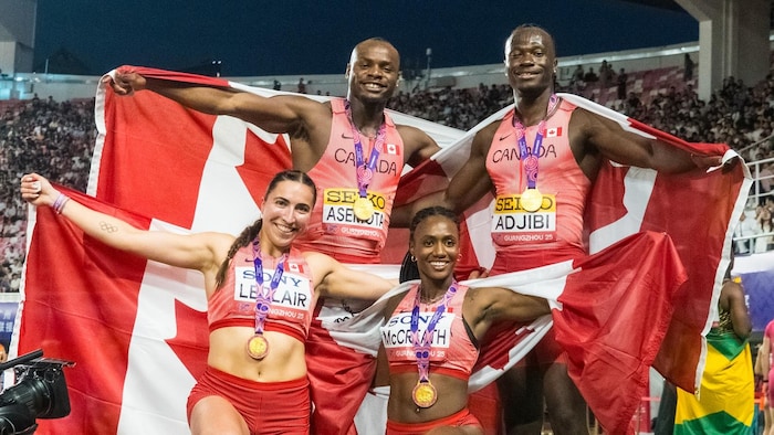 Quatre athlètes canadiens portent un drapeau sur leurs épaules et une médaille au cou.